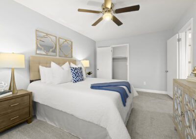 A serene bedroom scene showcasing a ceiling fan, side table with lamp and a well-arranged bed